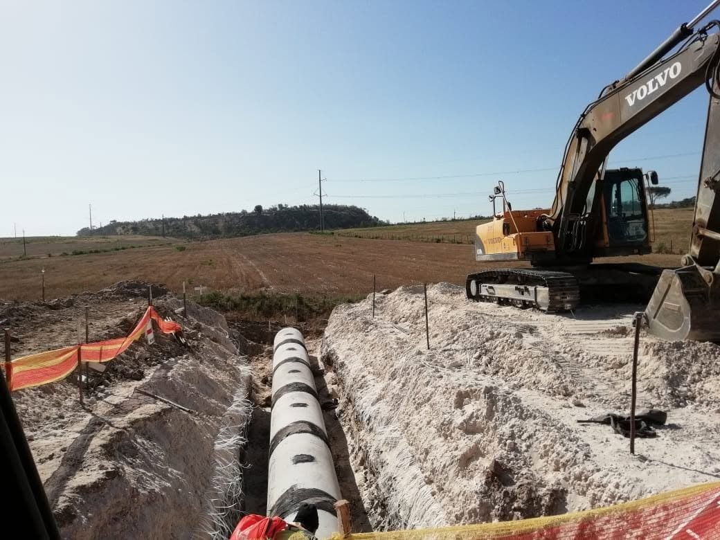 An excavator beside a bulk pipeline trench, with safety netting along the edge